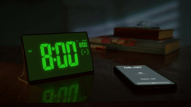 Digital alarm clock with green clockface and the smartphone waking up at 8 AM. The numbers on the clock screen changes from 7:59 no 8:00 AM. And the alarm goes off on the phone. Close up view.