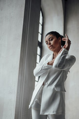 Portrait of candid authentic sexy mixed race model girl in white pantsuit posing hand on face