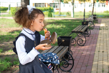 Girl with backpack eating sandwich packed in a sandwich box near school. A quick snack with a bun, unhealthy food, lunch from school. Back to school. Education, primary school classes, September 1