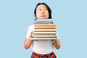 Young Asian woman holding a pile of books puffing cheeks with funny face. mouth inflated with air, catching air.
