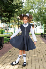 Cheerful funny girl with a toothless smile in a school uniform with white bows in school yard. Back...