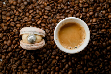 Selective focus of white cup with coffee and macaroon on top of fresh roasted coffee beans