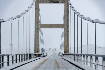 Driver’s perspective view on suspension bridge over Jökulsá river that connects the glacier lagoon Jokulsarlon with the sea during heavy snow storm and bridge covered in snow and snow clouds in sky