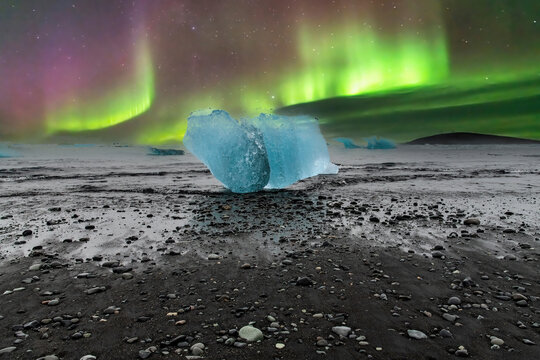 Low angle close up view during Aurora Borealis or Northern Lights of some large chunks of blue glacial ice coming from the Jokulsarlon glacier in Iceland on the volcanic black sand of Diamond Beach - Powered by Adobe