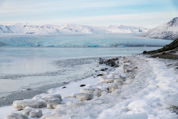 Panoramic view over the end or terminus of the Jokulsarlon glacier, Iceland and the frozen glacial lagoon with in forefront snow and ice at the edge of the lake
