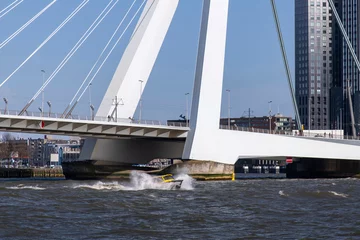 Photo sur Plexiglas Pont Érasme View over the Maas River in Rotterdam, the Netherlands, towards a small boat splashing water sideways in choppy water with the bridge close in the background
