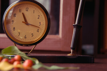 Vintage desk clock with ink fountain pen and apple tree leaves with small apples on wooden...