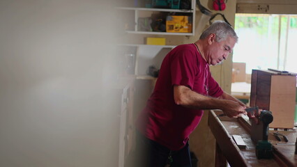 Fototapeta na wymiar Older man working at workshop, grabbing tools from wall and engaged with craftsmanship work hobby. Senior elderly worker