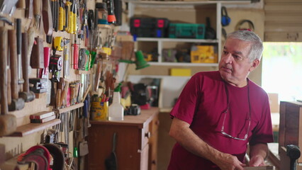 Senior man organizing tools hanging on wall at workshop carpentry shop