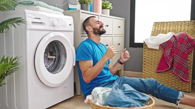 Young hispanic man waiting for washing machine dancing at laundry room