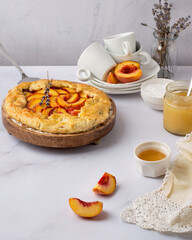 A biscuit on a stand, on the background of a saucer and a cup, a jar of honey, powdered sugar, peach slices, lavender sprigs..