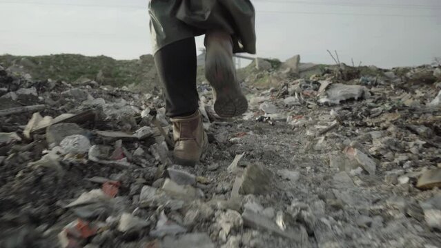 A woman in leather shoes and a raincoat walks through the dump.