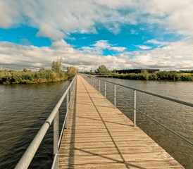 Fototapeta premium Footbridge over the canal system in Kinderdijk, Netherlands. In the distance, the iconic and historical Dutch windmills can be seen. Kinderdijk has been a UNESCO World Heritage Site since 1997.