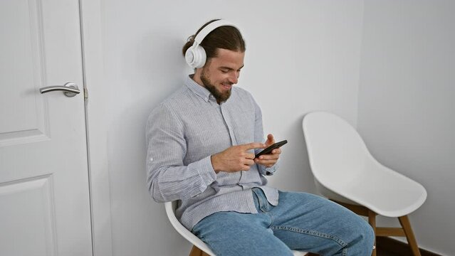 Young hispanic man using smartphone and headphones sitting on chair smiling at waiting room