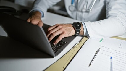Young hispanic man doctor using laptop stretching arms relaxing at the clinic