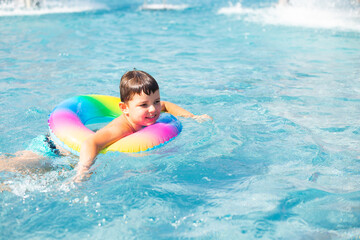 Fototapeta na wymiar Cute baby boy swims with a rainbow inflatable ring in a clean pool