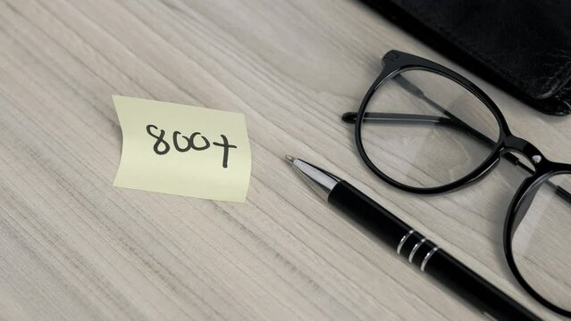 sticking a yellow sticky note with the inscription "800+" on a wooden tabletop, glasses and a wallet next to it (selective focus)