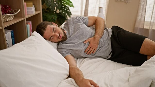 Young hispanic man suffering for stomach ache lying on bed at bedroom
