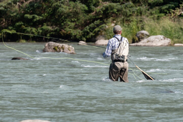Fly fisherman fishing in the middle of the river on a summer day.