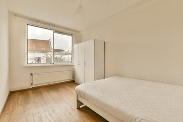 a bedroom with wood flooring and a white bed in front of a large window looking out onto the street
