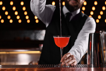 Bartender preparing fresh Martini cocktail in glass at bar counter, closeup