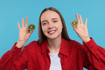 Young woman holding halves of kiwi on light blue background
