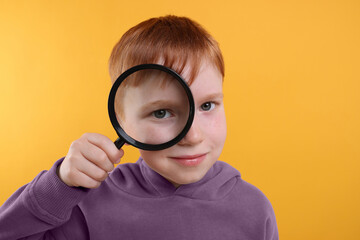 Boy looking through magnifier glass on yellow background