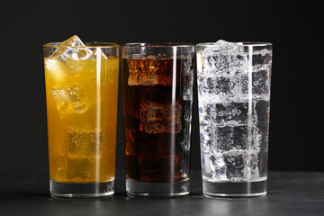 Glasses of different refreshing soda water with ice cubes on grey table