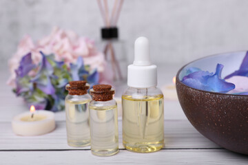 Spa composition. Bottles of essential oil and aromatic water with flowers in bowl on white wooden table, closeup