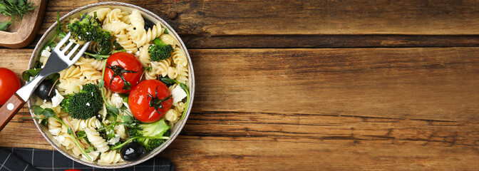 Bowl of delicious pasta with tomatoes, broccoli and cheese on wooden table, flat lay. Banner design with space for text