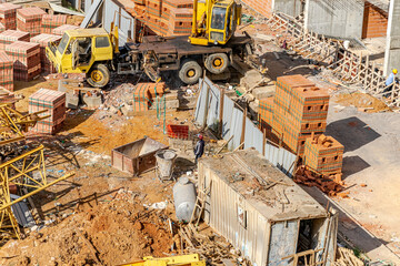 Aerial view of a messy construction site with unrecognizable people picking up red brick blocks...