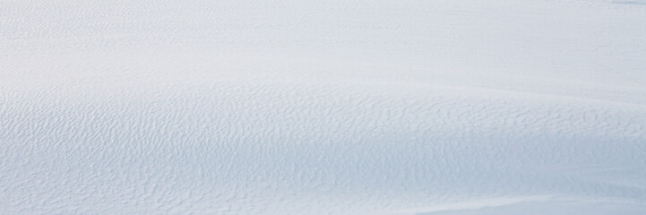 Beautiful winter background with snowy ground. Natural snow texture. Wind sculpted patterns on snow surface. Wide panoramic texture for background and design.