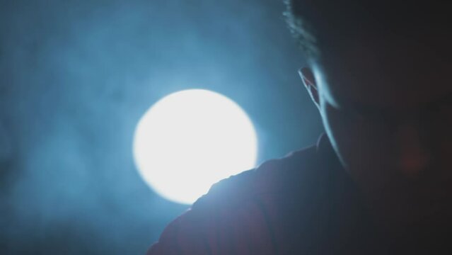 Film-like dolly shot of a man in a red shirt sitting on a table preparing for a stealth mission packing his weapons and knives with creative dramatic lighting technique, HD - 24 fps - Prores