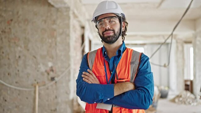 Young hispanic man architect standing with arms crossed gesture and serious face at construction site