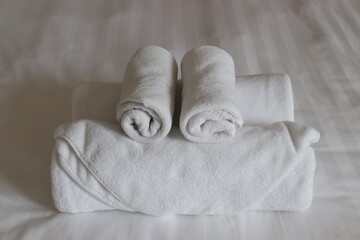 white rolled cotton towels stacked on white bed