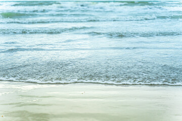 Fototapeta na wymiar The gentle lapping of the sea's soft waves creates a soothing ambiance along the tranquil sandy beach, enhanced by a soft focus that captures the serene beauty of the scene.