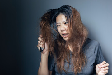 Fototapeta premium Asian girl with a comb and problem hair on gray background. Asian young woman holding brush, hairbrush with long loss hair problem after brushing.