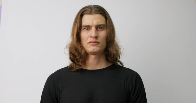 frawning young man looking at the camera with serious expresion standing posing in studio isolated gray background Slow motion