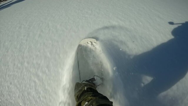 First Person POV of Person Snowboarding Fast on Ski Slope Mountain. Person snowboarder snowboarding down slope closeup with view white powder snow - winter extreme sports background.