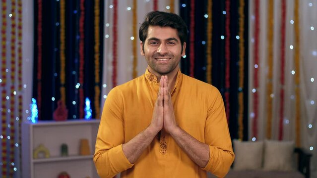Young Indian man greeting with namaste gesture - greeting guests at home  Asian man  Atithi Devo Bhava. Bokeh shot of handsome Indian guy happily joining hands in a namaste gesture - Diwali festiva...