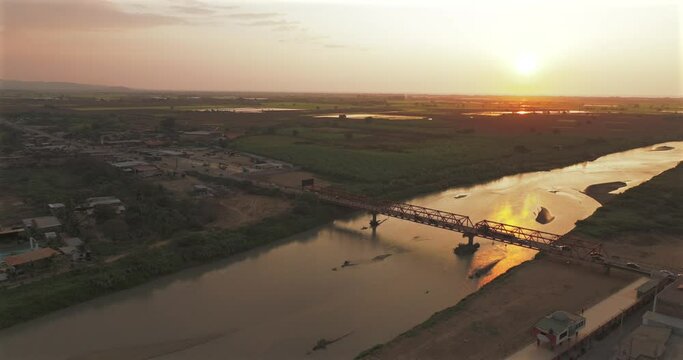 Aerial shot of Tumbes river, bridge and city at sunset. Tropical city at north of Per&uacute;. 