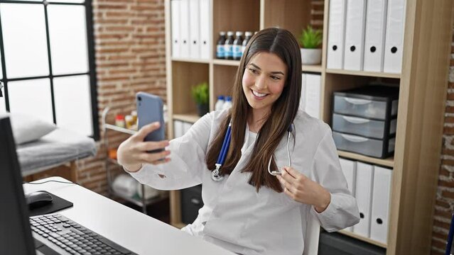 Young beautiful hispanic woman doctor make selfie by smartphone smiling at the clinic