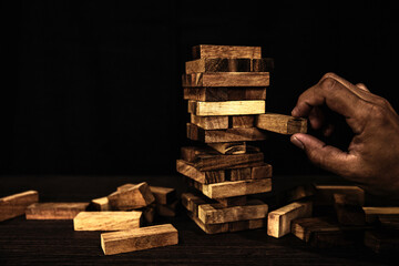 Hand placing wooden block stack in pyramid falling tower caution to prevent collapse or crash...