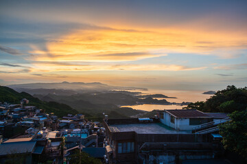 Stunning dusk scenery - vibrant orange sky, dynamic clouds, misty mountains. Serene Ocean Surrounding the Coastal Village of Jiufen in Taiwan.