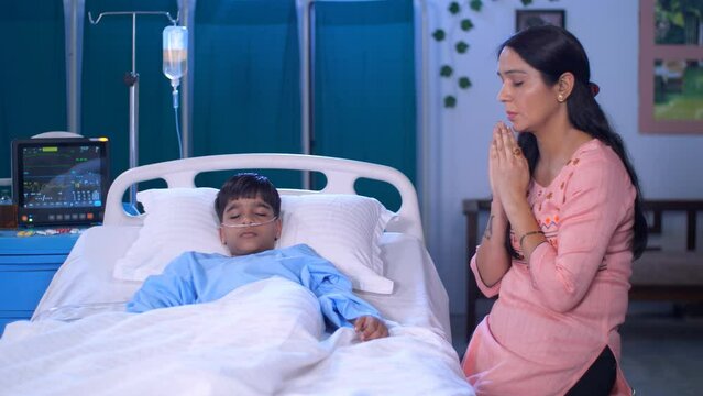 A worried Indian mother prays for her sick son in the hospital - speedy recovery  faith and belief  home hospital. A young boy and his caring mother in the hospital - family support  single parent ...