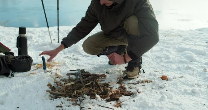 active handsome hicker lightning tree bark to make bonfire outdoors, spring holiday alone. traveler kindling fire on snowy ground Extreme travel. Survival in the wild. wildlife Harvesting wood