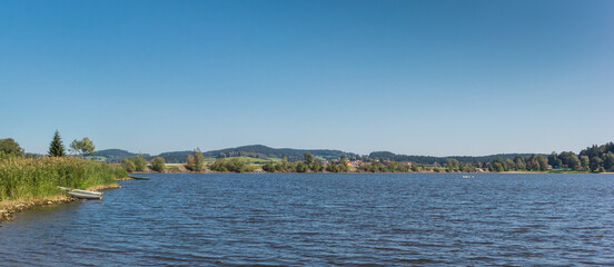 Obraz premium Panorama of a little rowing boat at the shore of lake Lipno in the Sumava mountains, Czech Republic
