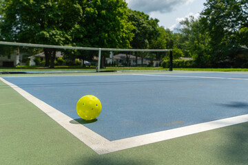 Recreational sport of pickleball court and ball in the United States with green and blue court with yellow ball on line.