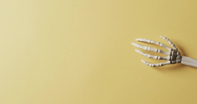 Video of halloween skeleton hands with copy space on yellow background