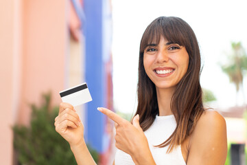 Young woman holding a credit card at outdoors and pointing it